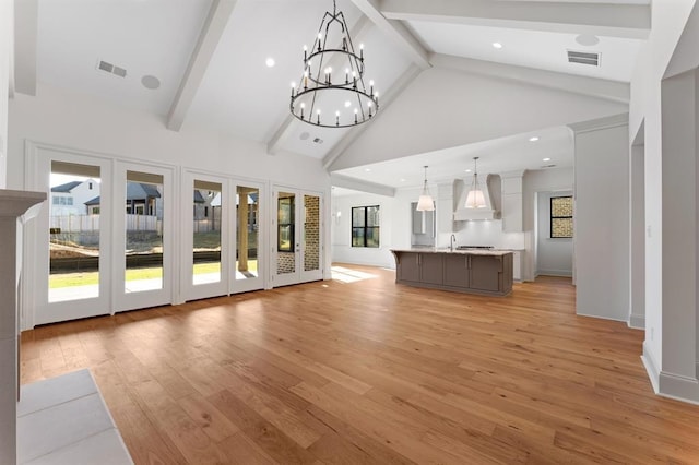 unfurnished living room featuring high vaulted ceiling, beamed ceiling, a chandelier, sink, and light hardwood / wood-style floors