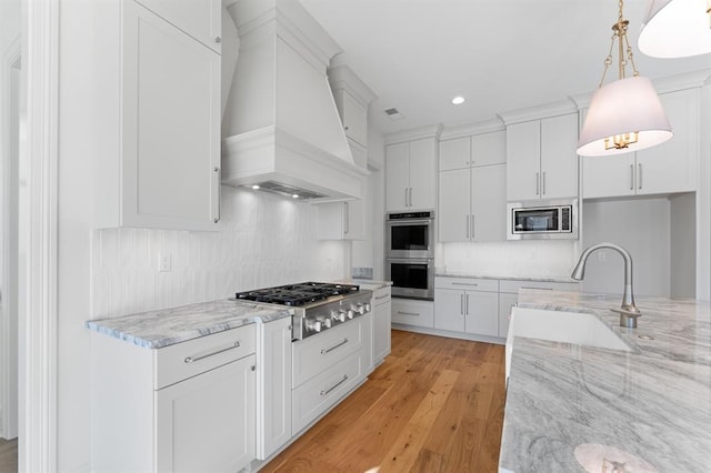 kitchen with premium range hood, stainless steel appliances, light hardwood / wood-style floors, and white cabinetry