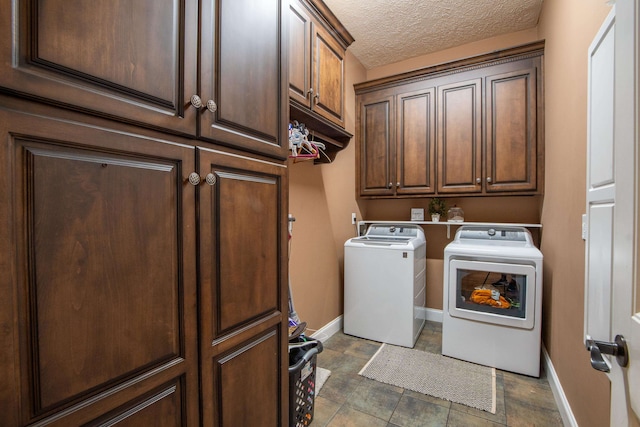 laundry room with dark tile flooring, washing machine and clothes dryer, cabinets, and a textured ceiling