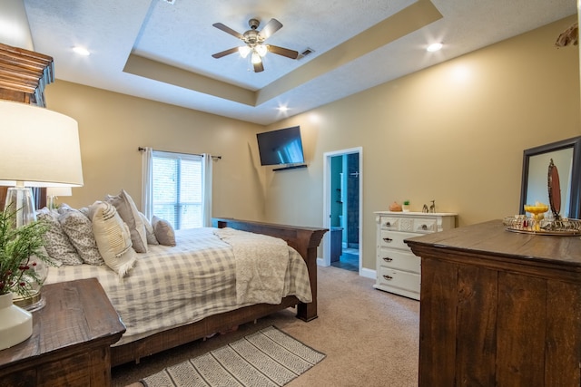 carpeted bedroom with a textured ceiling, a raised ceiling, ceiling fan, and connected bathroom