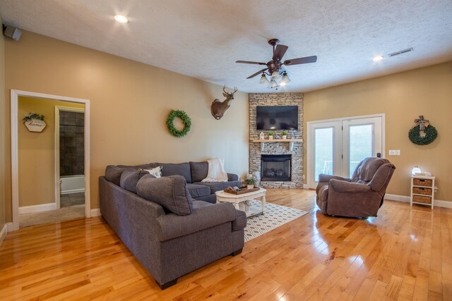 living room featuring ceiling fan, light hardwood / wood-style flooring, a fireplace, a textured ceiling, and french doors