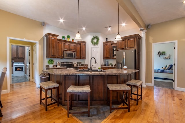 kitchen with sink, light wood-type flooring, hanging light fixtures, stainless steel appliances, and a center island with sink