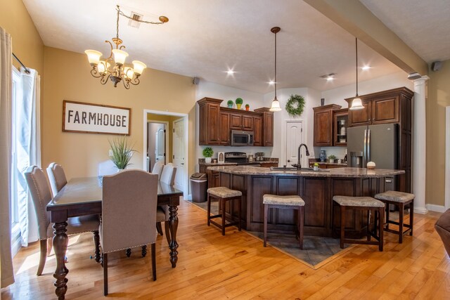 kitchen featuring decorative light fixtures, appliances with stainless steel finishes, an island with sink, and light hardwood / wood-style flooring