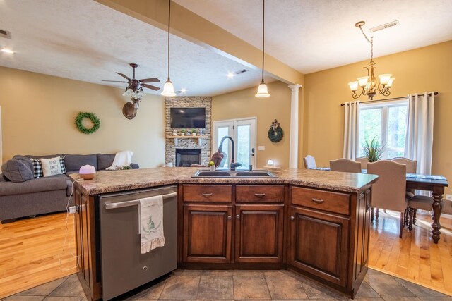 kitchen with decorative light fixtures, a stone fireplace, dishwasher, hardwood / wood-style flooring, and sink