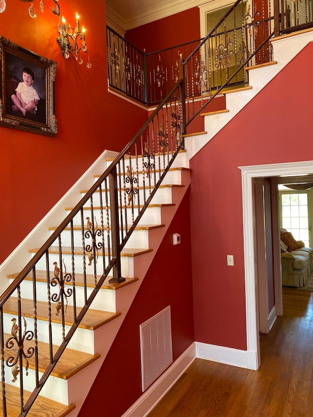 staircase featuring wood-type flooring, a high ceiling, ornamental molding, and an inviting chandelier