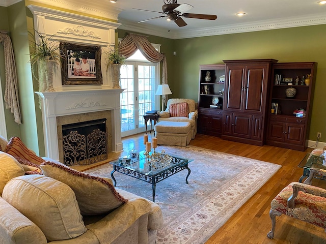 living room featuring a premium fireplace, hardwood / wood-style flooring, ornamental molding, and ceiling fan