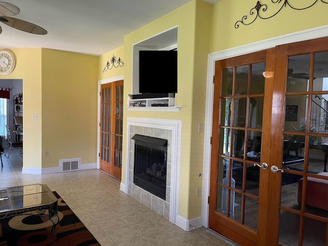 living room with ceiling fan, light tile patterned floors, a tile fireplace, and french doors