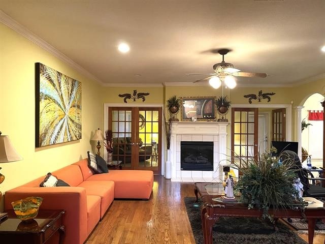 living room featuring a fireplace, light wood-type flooring, french doors, ceiling fan, and crown molding