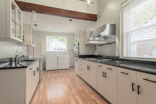 kitchen featuring pendant lighting, light wood-type flooring, washer and clothes dryer, wall chimney range hood, and dark stone countertops