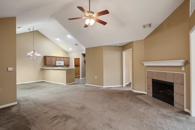 unfurnished living room with ceiling fan with notable chandelier, a tiled fireplace, light carpet, and high vaulted ceiling