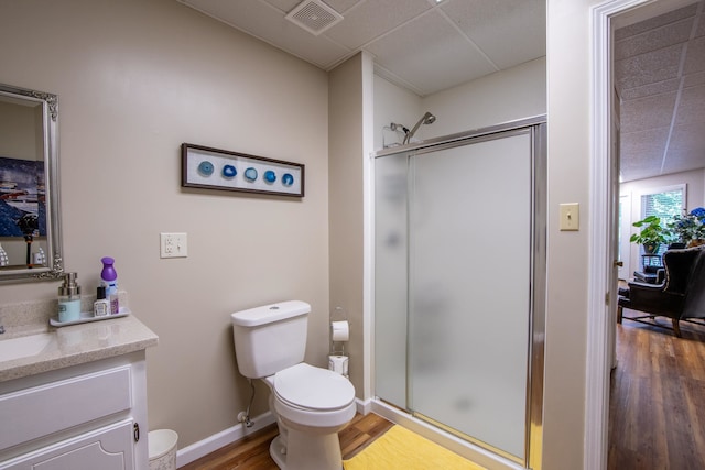 bathroom featuring a paneled ceiling, vanity with extensive cabinet space, walk in shower, toilet, and wood-type flooring