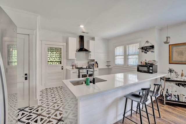 kitchen with white cabinets, kitchen peninsula, a kitchen bar, and wall chimney range hood