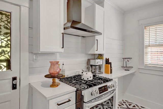 kitchen featuring ornamental molding, wall chimney exhaust hood, stainless steel range with gas cooktop, and white cabinetry