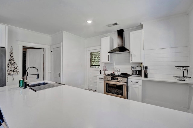 kitchen featuring sink, wall chimney range hood, white cabinetry, stainless steel stove, and decorative backsplash