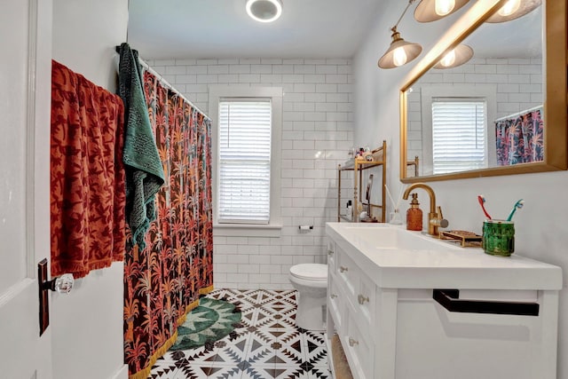 bathroom with vanity, tile walls, toilet, and a healthy amount of sunlight