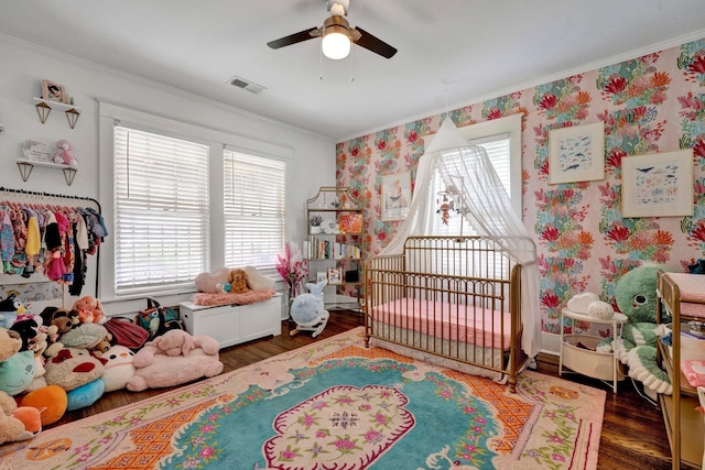 bedroom with crown molding, ceiling fan, dark wood-type flooring, and a nursery area