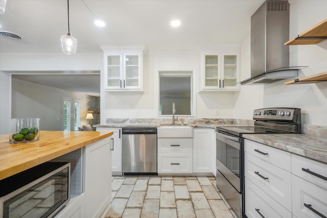 kitchen with stainless steel appliances, butcher block counters, sink, wall chimney exhaust hood, and white cabinetry