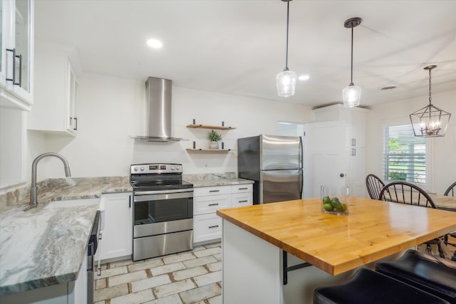 kitchen with stainless steel appliances, hanging light fixtures, wall chimney exhaust hood, white cabinets, and sink