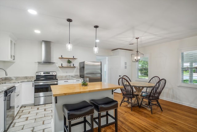 kitchen featuring stainless steel appliances, wall chimney range hood, light hardwood / wood-style floors, and white cabinets