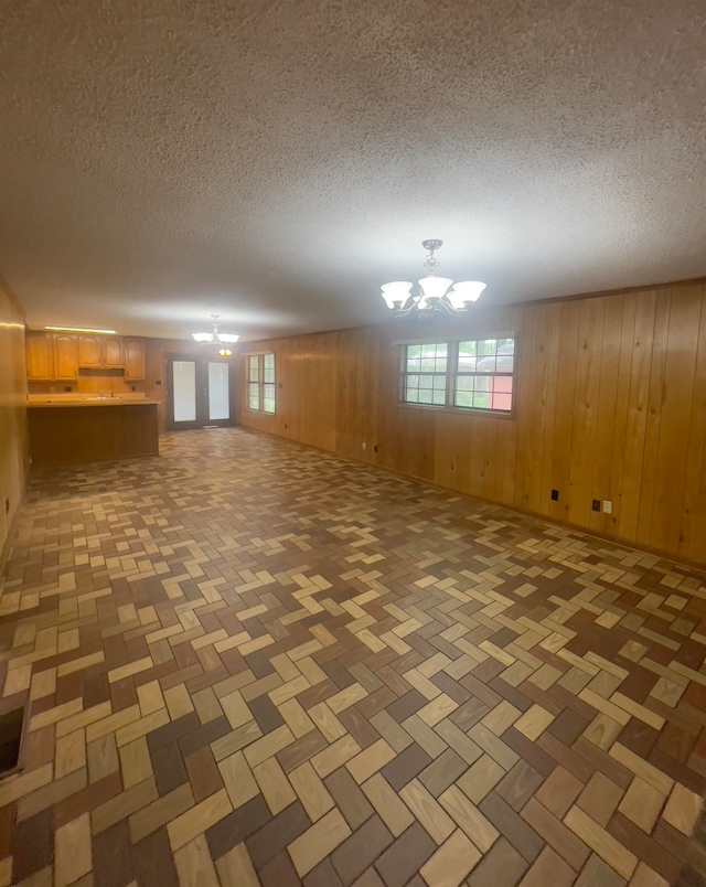 basement featuring a notable chandelier, dark parquet floors, wooden walls, and a textured ceiling