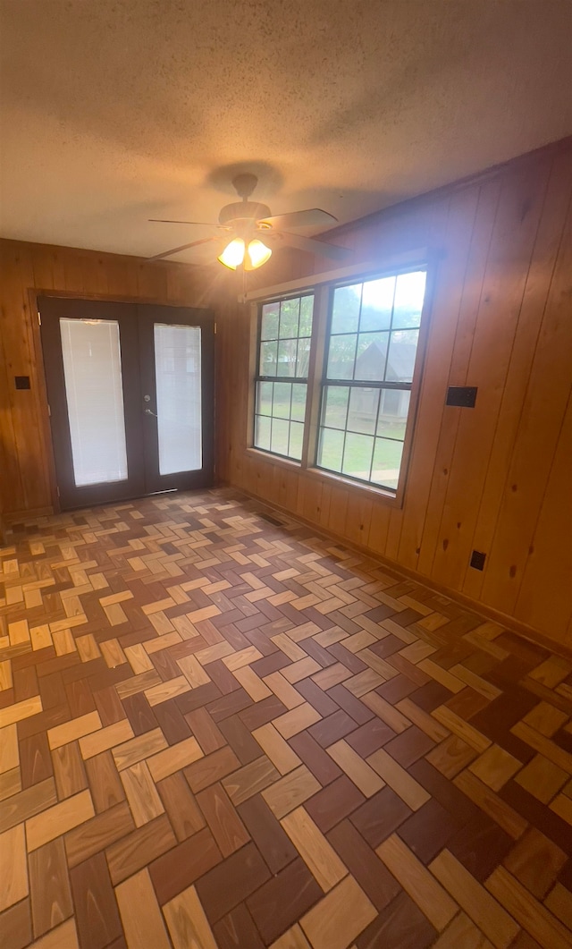 spare room featuring parquet floors, wooden walls, ceiling fan, and a textured ceiling