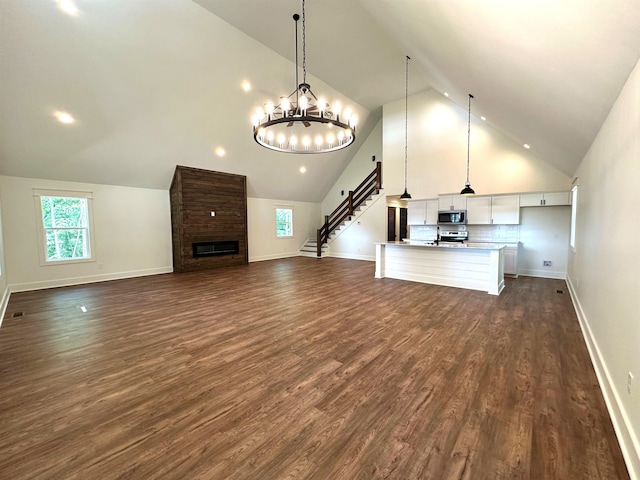 unfurnished living room featuring brick wall, an inviting chandelier, hardwood / wood-style flooring, a brick fireplace, and high vaulted ceiling