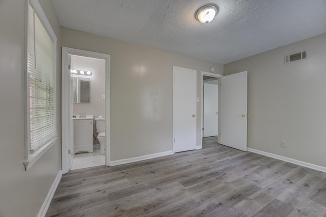 unfurnished bedroom with sink, a textured ceiling, ensuite bathroom, and hardwood / wood-style flooring