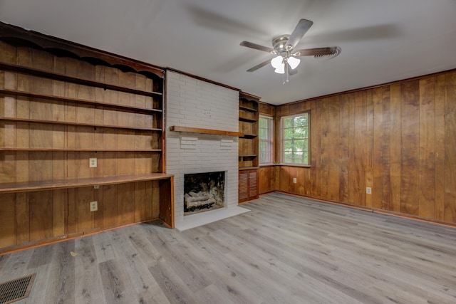 unfurnished living room featuring light hardwood / wood-style floors, brick wall, a brick fireplace, wood walls, and ceiling fan