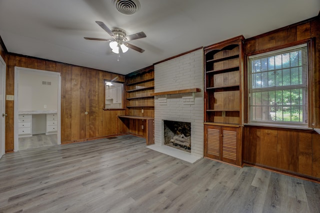 unfurnished living room featuring wooden walls, ceiling fan, light wood-type flooring, and a brick fireplace