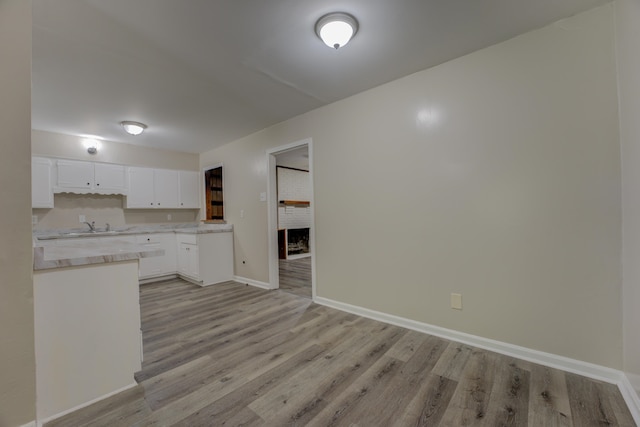 kitchen with sink, light hardwood / wood-style floors, a fireplace, and white cabinetry