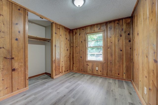 unfurnished bedroom with wood walls, a closet, a textured ceiling, and light wood-type flooring