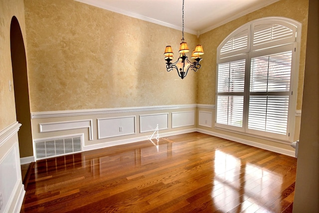 empty room featuring crown molding, hardwood / wood-style floors, and a chandelier