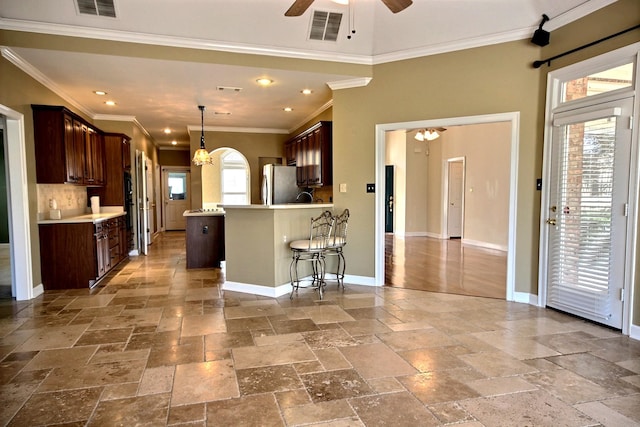 kitchen with a healthy amount of sunlight, ceiling fan with notable chandelier, stainless steel refrigerator, and ornamental molding