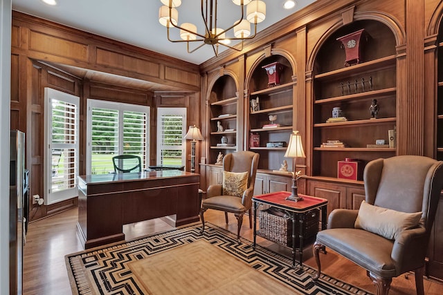 office area with a chandelier, ornamental molding, wood-type flooring, built in shelves, and wooden walls