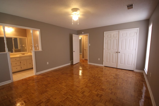 unfurnished bedroom with ceiling fan, ensuite bathroom, a textured ceiling, light tile floors, and sink