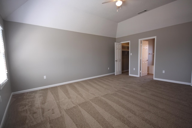 unfurnished bedroom featuring carpet flooring, vaulted ceiling, ceiling fan, a walk in closet, and ensuite bath