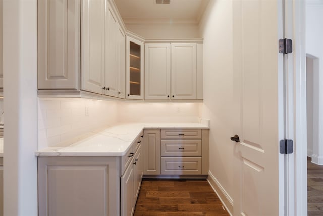 kitchen featuring crown molding, dark wood-type flooring, light stone counters, and backsplash