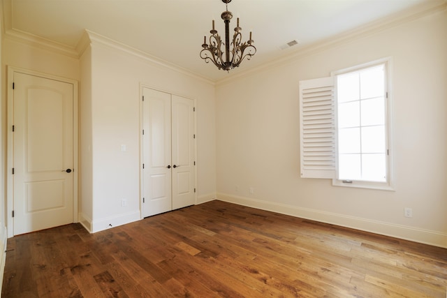 unfurnished bedroom with ornamental molding, a closet, a chandelier, and wood-type flooring