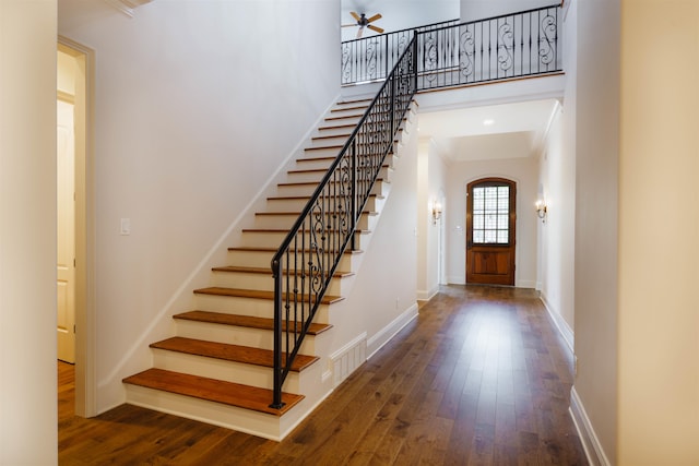 entryway featuring ornamental molding, a towering ceiling, and dark wood-type flooring