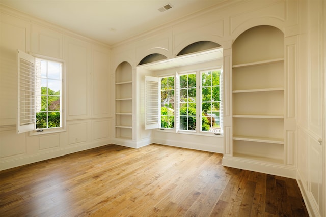 empty room featuring light hardwood / wood-style floors, ornamental molding, and built in shelves