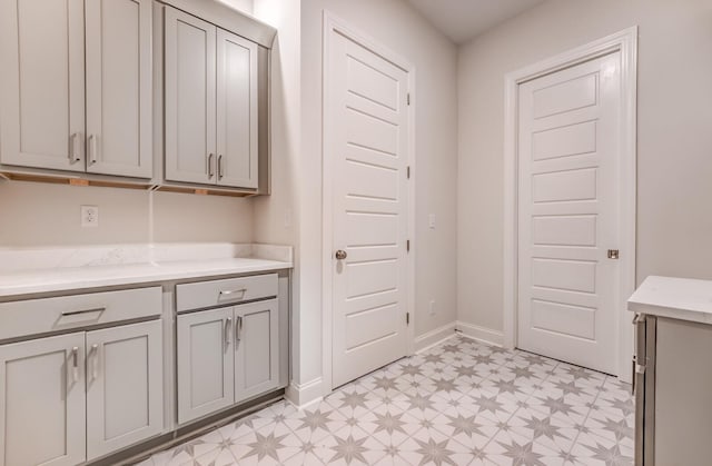 interior space with baseboards, light floors, light stone counters, and gray cabinetry