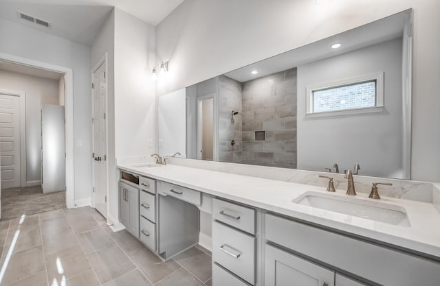 bathroom with double vanity, visible vents, a tile shower, and a sink