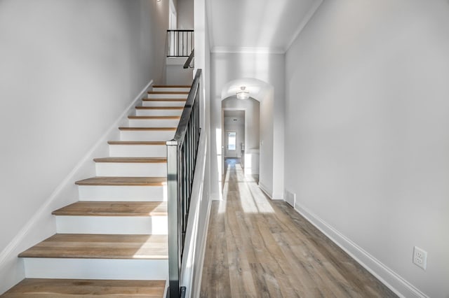 stairway with arched walkways, visible vents, ornamental molding, wood finished floors, and baseboards