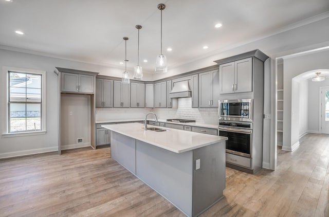 kitchen with arched walkways, appliances with stainless steel finishes, gray cabinetry, premium range hood, and a sink