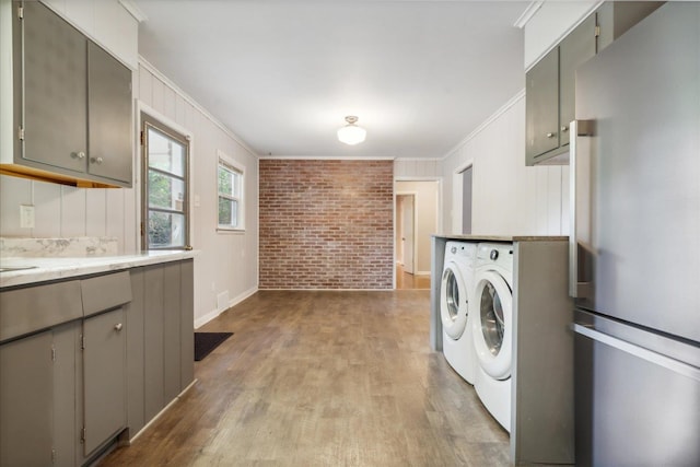 washroom featuring separate washer and dryer, ornamental molding, brick wall, and hardwood / wood-style floors