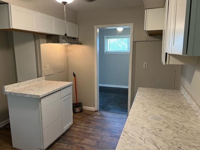 kitchen with light stone counters, white cabinetry, and dark hardwood / wood-style floors