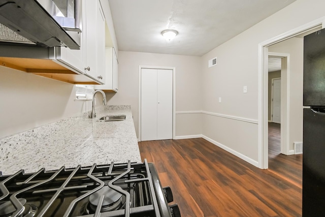 kitchen with white cabinets, black refrigerator, sink, light stone counters, and dark hardwood / wood-style flooring