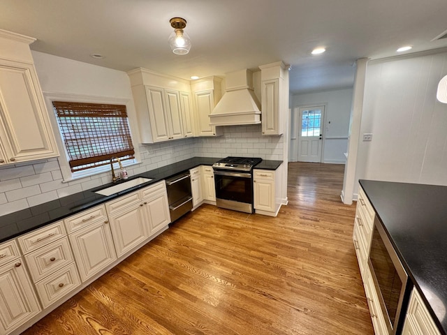 kitchen featuring light wood-type flooring, tasteful backsplash, custom range hood, stainless steel appliances, and sink