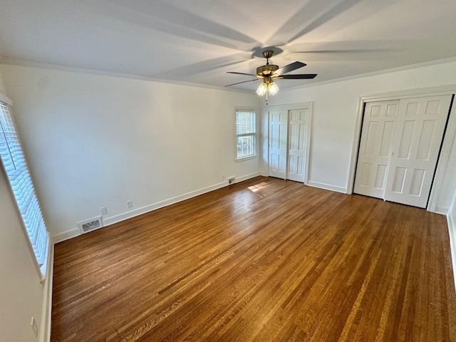 unfurnished bedroom with hardwood / wood-style flooring, crown molding, ceiling fan, and multiple closets