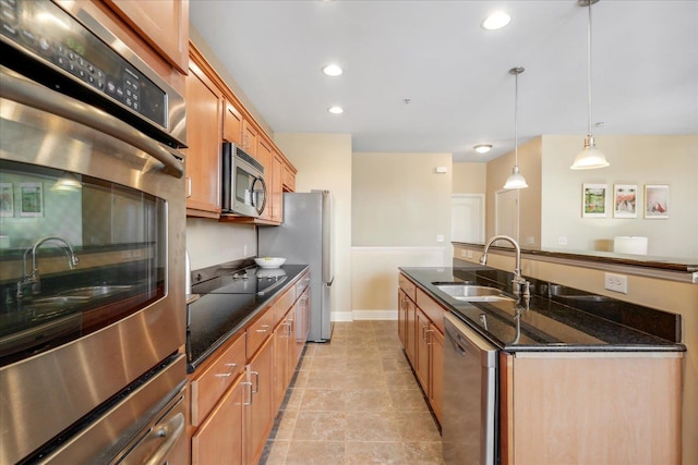 kitchen featuring stainless steel appliances, hanging light fixtures, a sink, dark stone countertops, and an island with sink